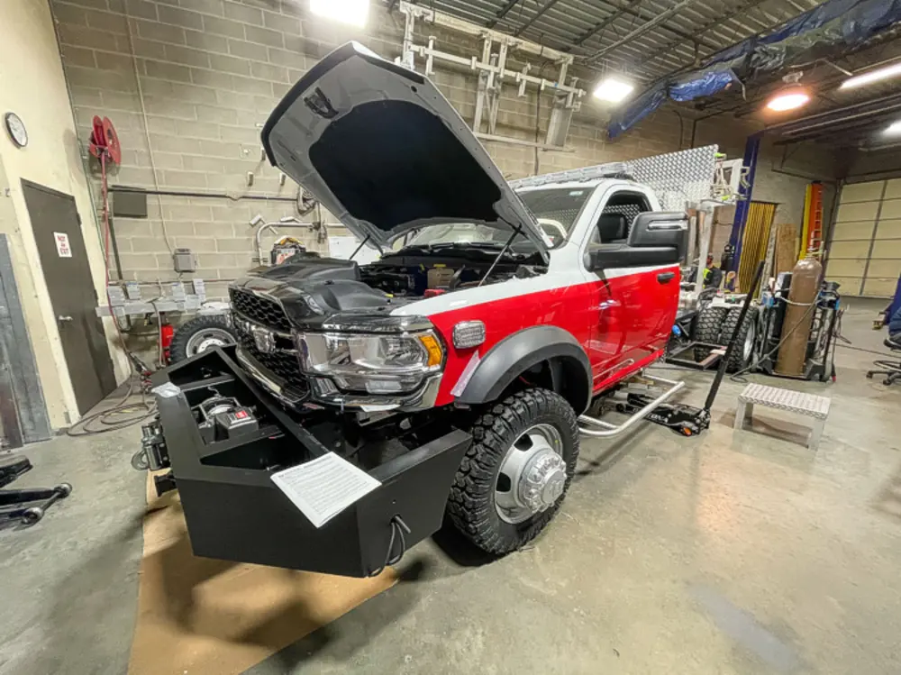 Exterior view of small fire truck showing cab, body compartments, and wheel/tire area.